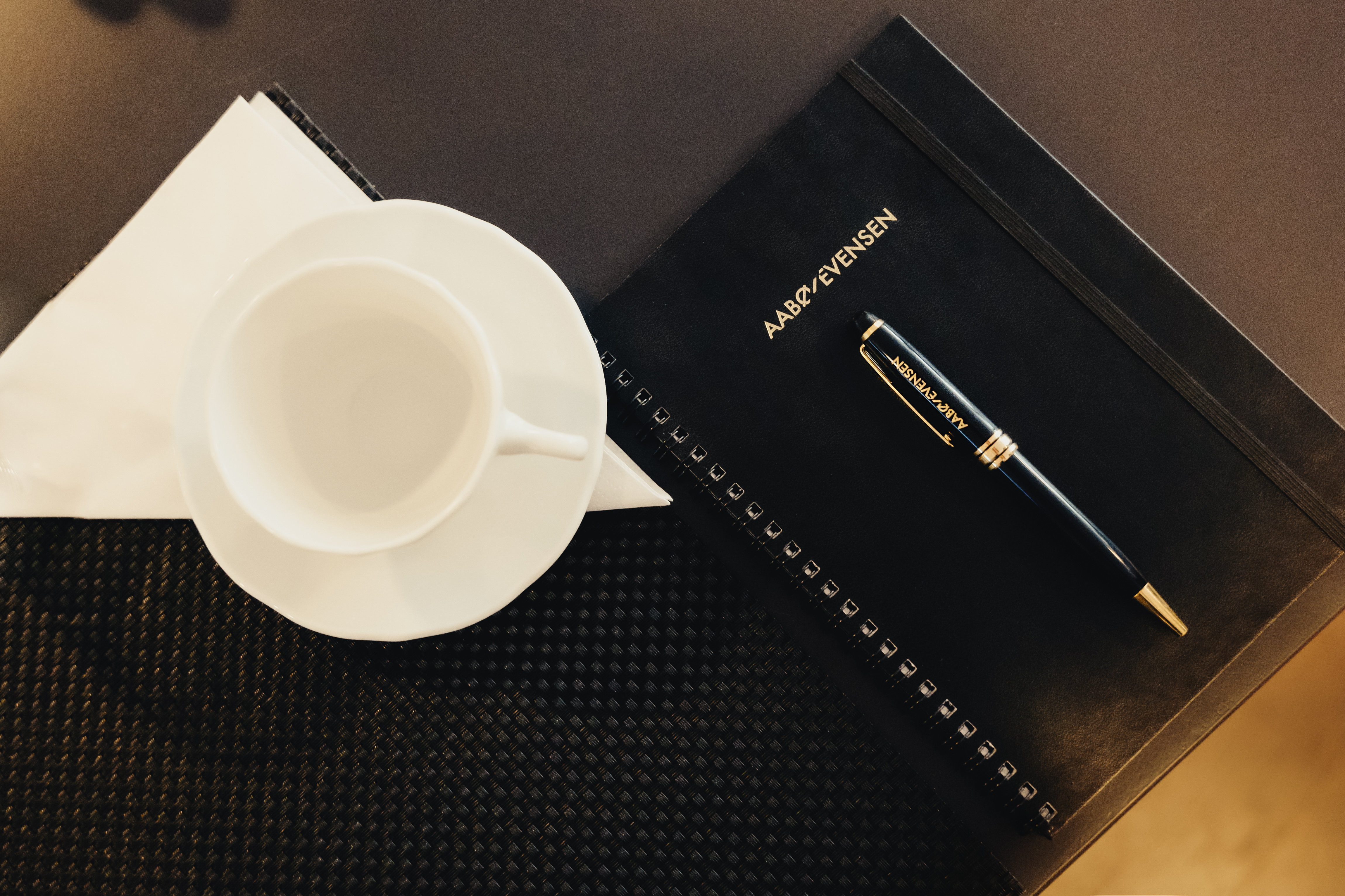 Tom kaffekopp og bok og penn med Aabø-Evensen-logo